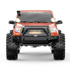 Orange RC rock crawler front view with lit headlights, black bumper guard, knobby tires