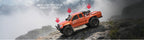 Orange RC rock crawler truck on rocky slope with suspension arrows